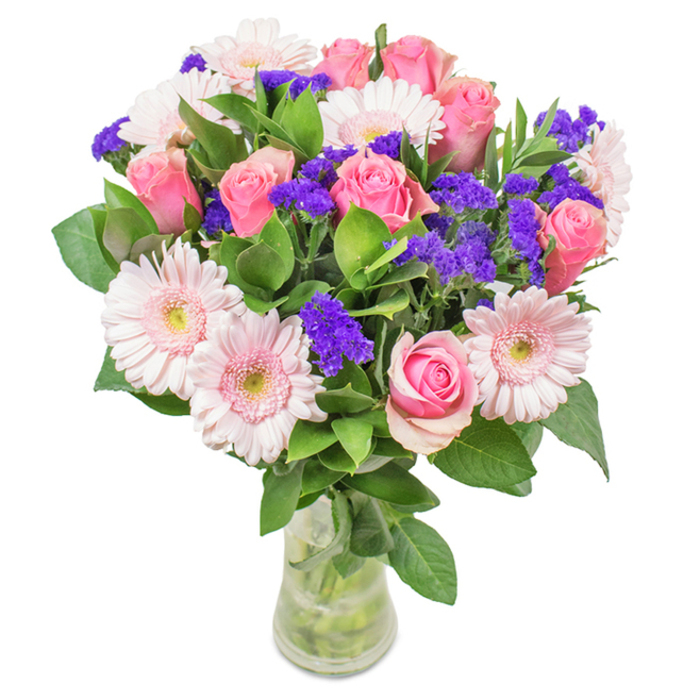 This elegant, locally inspired bouquet-artfully arranged in a sleek, clear glass vase-showcases Carshalton's affinity for soft, romantic color and natural abundance. At its heart are approximately seven to nine medium pink roses, some tightly furled, others just beginning to open, their signature spiral shapes reminiscent of heritage blooms from Carshalton's historic gardens. Five to seven pale pink Gerbera daisies add expanses of gentle color, each large-headed and petal-rich, their nearly white centers brightening the arrangement with subtle grace. Threaded throughout are vibrant clusters of vivid purple statice, which offer a pleasing texture and visual depth, echoing the wild flora of Carshalton Park. The bouquet's deep green foliage anchors the overall composition, infusing it with freshness and evoking the lushness of the local landscape. The transparent vase displays the sturdy green stems and pure water, underscoring the just-gathered look prized by discerning Carshalton residents. This arrangement, perfect for birthdays, anniversaries, or to mark joyous occasions, brings together the beloved flowers of the area to convey celebration, appreciation, and affection-delivered with the signature care of Carshalton's expert florists.